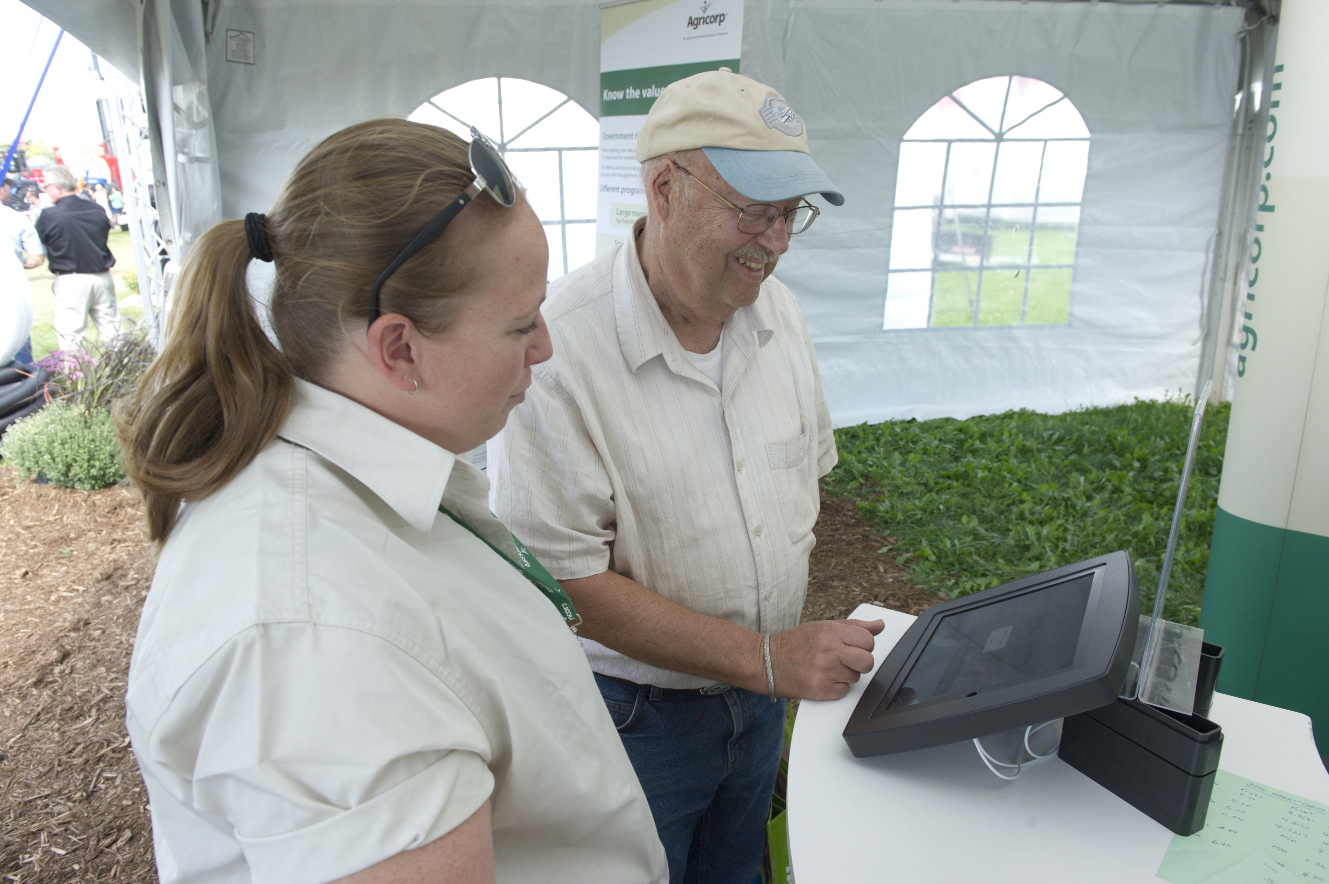 Un employé d’Agricorp aide un producteur à se servir de l’outil Kiosk pour accéder à de l’information lors d’une exposition agricole.