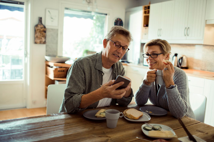 Un homme et une femme prennent le petit-déjeuner tout en regardant l'écran de leur téléphone intelligent